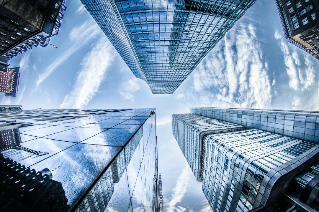 Ground view of looking upwards towards buildings in the city, where the buildings glass outlines mirror the clouds in the sky