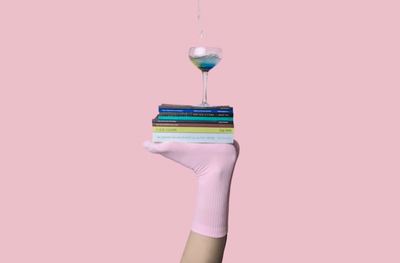 Image of a sock-clad foot attempting to balance a wine glass on top of a pile of books