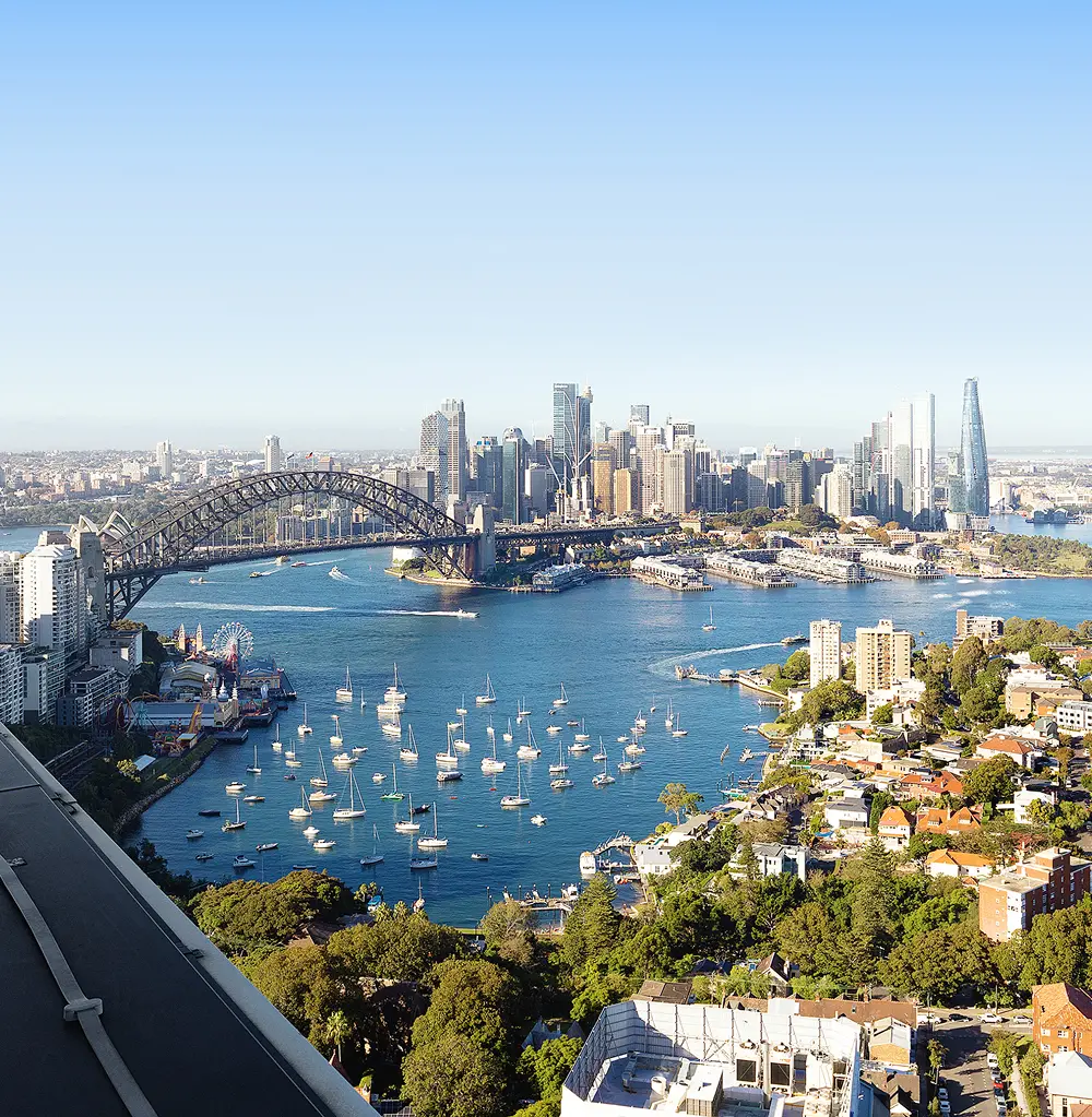The Sydney Harbour Bridge spans a vibrant blue bay dotted with moored sailboats, stretching toward a dense city skyline of tall skyscrapers under a clear, bright sky.