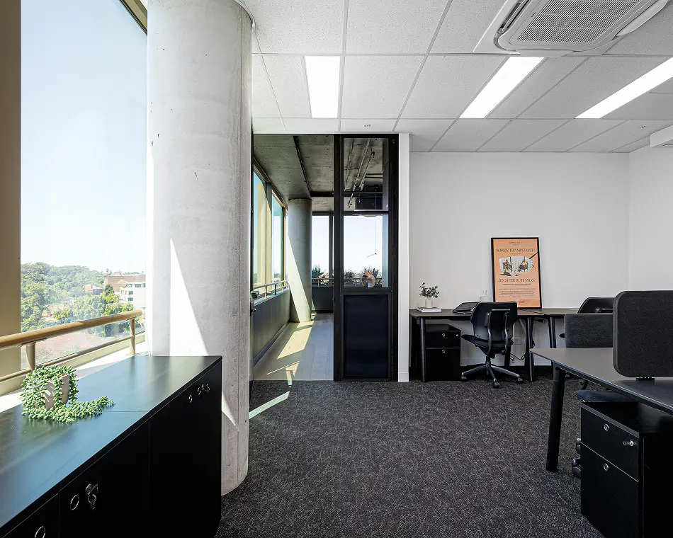 A modern office space featuring black desks and office chairs stands illuminated by natural light beside large floor-to-ceiling windows and a prominent concrete support pillar. Poster text reads: "COMMON FOLK PRESENTS SOREN TRAMPEDACH FOUNDER WORKCLUB GLOBAL JENNIFER ROBINSON HUMAN RIGHTS LAWYER AND BARRISTER"