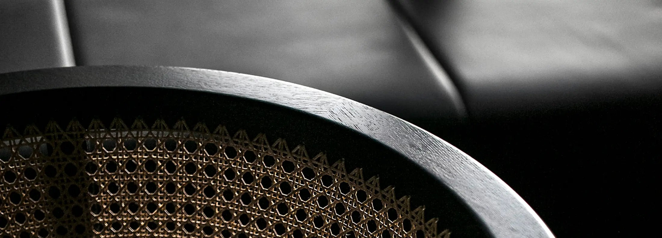 A dark wooden circular frame with a woven cane mesh sits in the foreground, catching soft light against a background of dark leather furniture.