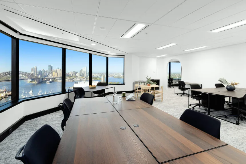 Large private office with a long boardroom table and black chairs, wide corner windows overlooking Sydney Harbour and the Harbour Bridge.