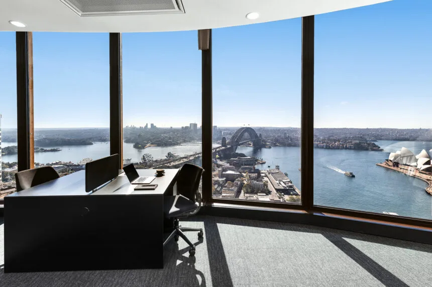 Small private office with two black desks and chairs beside floor-to-ceiling windows overlooking Sydney Harbour and the Opera House.