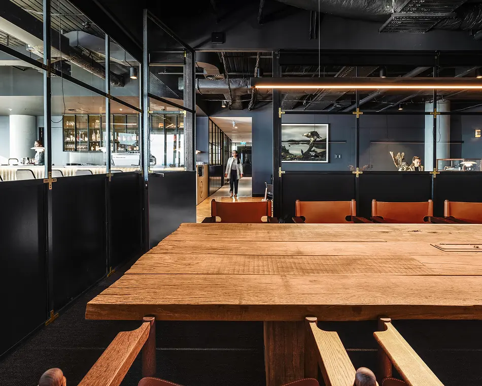 Long timber table beside black-framed glass meeting rooms