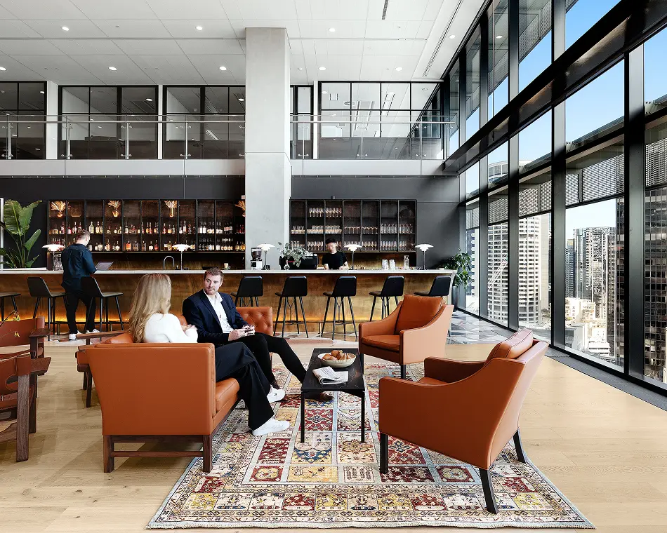 Members relaxing in a lounge with orange armchairs, a bar and floor-to-ceiling windows