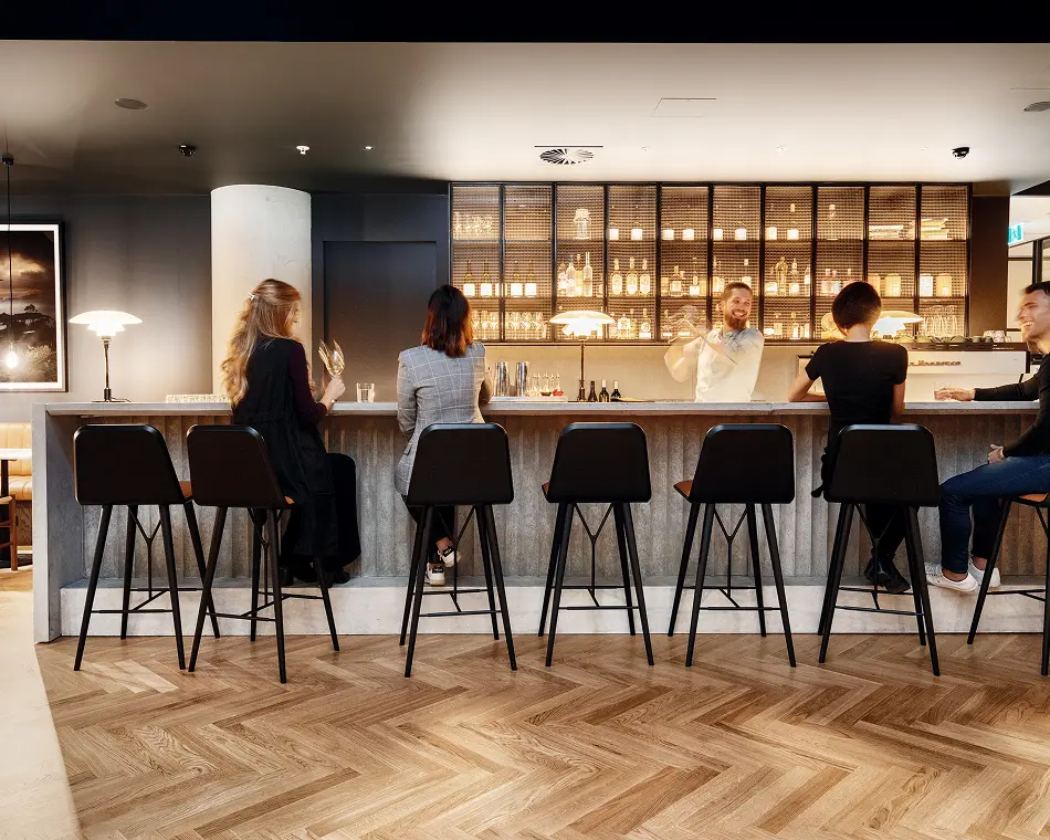 Members at the lounge bar counter with black stools and glassware shelving behind
