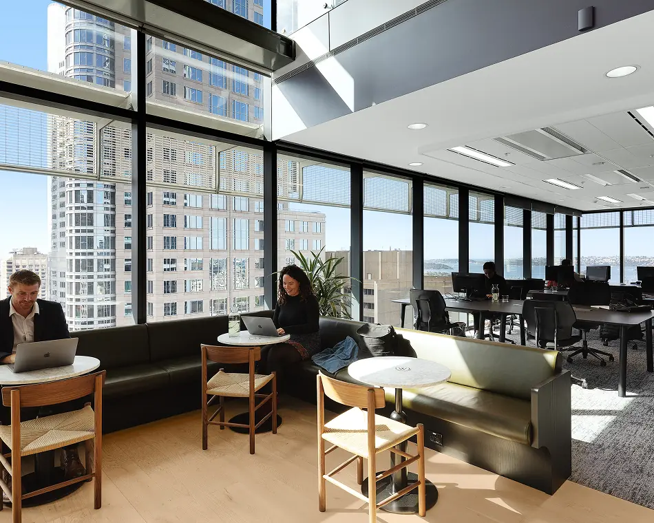 Members working on laptops in a coworking lounge with round tables and floor-to-ceiling windows