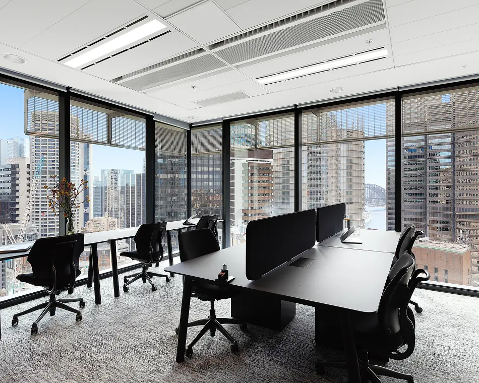Bright corner office with desks, ergonomic chairs and floor-to-ceiling city and harbour views